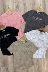 Remera blanca con estampado tie-dye en tonos grises y logo "LOU JEANS" con apliques brillantes.