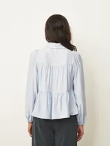 Camisa de corte amplio y estilo romántico, color celeste, con cuello clásico, cierre frontal de botones y diseño de canesú fruncido. Presenta mangas largas abullonadas con puños elásticos.