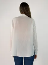 Camisa de corte oversize color beige, con cuello clásico, cierre frontal de botones y detalle de flores de tela aplicadas en el pecho.