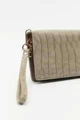 Billetera de mano con textura efecto cocodrilo, color beige, con cierre perimetral y tira de muñeca desmontable.