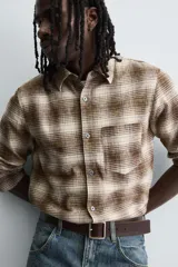 Camisa de corte relajado confeccionada en tejido de algodón con estampado de cuadros en tonos marrones y beige. Presenta cuello solapa, manga larga con puños abotonados, bolsillo plastrón en el pecho y cierre frontal con botones.