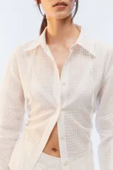 Camisa oversize negra de algodón liviano con textura calada, cuello camisero, botones frontales, mangas largas voluminosas y tiras para anudar en la espalda.