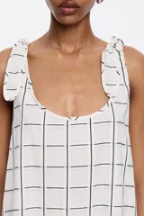 Vestido largo blanco con estampado de líneas negras formando un patrón de cuadrícula. Tiene tirantes anchos con detalle de lazo en los hombros, escote redondo pronunciado en delantero y espalda, y corte línea A.