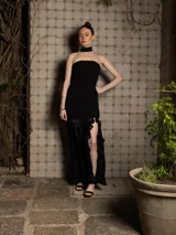 Vestido largo negro con cuerpo fruncido strapless, falda con tajo lateral y volados transparentes.