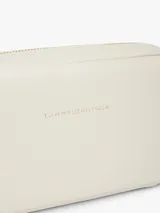 Cartera tipo bandolera de diseño compacto y líneas redondeadas, marca Tommy Hilfiger. Está confeccionada en poliuretano con acabado liso de color beige, cierre de cremallera y cuenta con una inscripción de la marca en bajo relieve en la parte delantera. Incluye una correa cruzada ajustable de jacquard tonal con el logo de la marca.