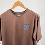 Remera marrón de mangas cortas con estampa en la espalda que incluye una flor azul, la frase "Boundless Art" y números.