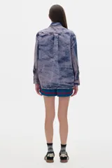 Camisa de jean azul con lavado gastado, corte oversized, manga larga y cierre frontal con botones.