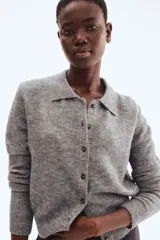 Cárdigan corto de punto suave, color gris jaspeado, con cuello camisero, abotonadura frontal y remates acanalados en puños y bajo.