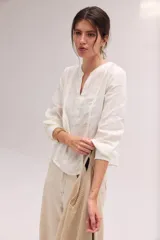 Blusa blanca de lino con escote en V y mangas largas con puños elásticos, combinando delantera estructurada de lino y espalda de algodón con spandex.