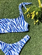 Conjunto de bikini con estampado de cebra en tonos azul y blanco. El corpiño es de un hombro y la bombacha es colaless.