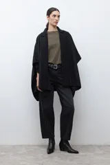Capa negra con solapa y cuello tejido, de corte amplio y sin mangas.