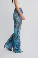 Jean de tiro medio y pierna flare de denim azul con estampa en toda la prenda y detalles de calados bordados florales en la parte inferior. Cuenta con cinco bolsillos y cierre frontal con cremallera.