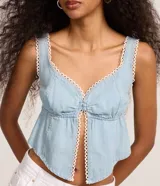 Blusa cropped de jeans en color Celeste, con escote corazón, tirantes anchos y cierre frontal con botones en el busto y abertura central. Presenta bordados picotados en los bordes.