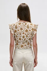 Blusa de diseño estampado con motivos florales y cachemira en tonos marrones sobre base blanca, con escote en V profundo y doble lazo frontal ajustable. Presenta mangas cortas con volados.