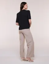 Blusa blanca de corte recto y tejido liviano de gasa con forro interno delantero. Presenta escote en V con cuello redondo y lazo central para anudar, mangas cortas con hilera de botones forrados en los laterales y ruedo ligeramente redondeado.
