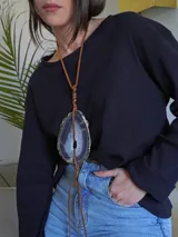 Collar con dije de piedra ágata blanca y marrón, con forma circular irregular y agujero en el centro. El dije está sujeto con un cordón fino de cuero marrón.