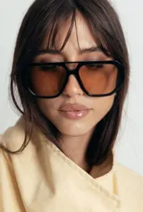 Lentes de sol con armazón de policarbonato negro y cristales tonalidad ámbar, con diseño de puente doble estilo aviador.