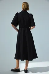 Vestido largo negro de popelina de algodón con alforzas, inserciones de encaje, manga corta abullonada, cuello camisero, botonadura frontal y cinturón fino para atar en la cintura.
