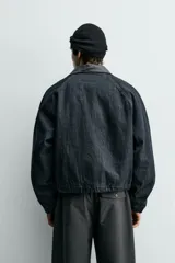 Cazadora de corte relajado confeccionada en tejido denim de algodón sin lavados, con ligero acolchado interior. Presenta cuello solapa en tejido efecto piel a contraste, cierre frontal de cremallera, bolsillos de vivo en la cadera y puños elásticos.