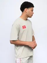 Remera de corte holgado en color beige, con cuello redondo y logo de Umbro estampado en un recuadro rojo sobre el pecho.