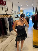 Top negro de tirantes finos con diseño en capas, presentando un volante de encaje en la parte superior y un bajo asimétrico con terminación en encaje.