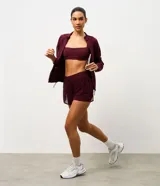 Bermuda deportiva femenina modelo runner, color bordó, con short interno incorporado. Presenta cintura elástica con cordón de ajuste y laterales con cordones ajustables. Confeccionada en tejido de tul con tecnología dry para mayor transpirabilidad.