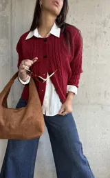 Cardigan de punto con textura trenzada en color bordó, con cuello redondo y cierre frontal mediante botones tipo alamar. Presenta mangas largas con puños acanalados y un corte clásico.