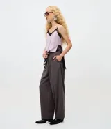 Pantalón de sastrería modelo barrel, de tiro alto y corte amplio con piernas anchas. Presenta pliegues frontales, trabillas para cinturón y recortes decorativos en la parte delantera.