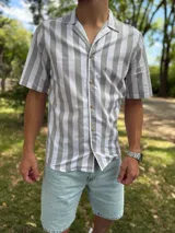 Camisa de manga corta con diseño de rayas verticales en tonos gris y blanco, cuello abierto estilo cubano y cierre frontal con botones de madera.