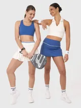 Conjunto deportivo compuesto por un top corto tipo polo sin mangas en color blanco y una pollera deportiva azul con cintura alta y detalle de vivo en contraste.