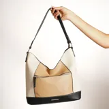 Bolso hobo de cuero sintético color beige, blanco y negro, con correa al hombro ajustable y bolsillo externo con cierre.