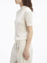 Sweater de lana merino color crema, de corte slim, cuello perkins y manga corta. Presenta detalles de puntadas en los hombros y ribetes de canalé en cuello, puños y bajo.