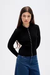 Remera de manga larga ajustada al cuerpo, confeccionada en tejido acanalado de color negro. Presenta cuello tipo polo y cierre frontal con una hilera de botones pequeños.