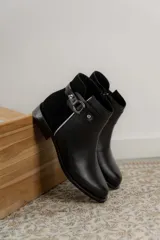 Botas cortas de cuero negro con paneles traseros de gamuza, cierre lateral y detalle de correa con hebilla metálica en el tobillo.