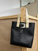 Bolso tipo tote bag negro con textura símil cuero de cocodrilo, doble asa corta color marrón y beige, y cierre con broche metálico con forma orgánica.