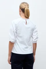 Remera blanca de manga tres cuartos, con cuello redondo y detalles de bordado calado en la parte frontal y hombros.