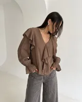 Blusa de color marrón con escote en V, mangas largas abullonadas con puños elásticos y detalles de volados en los hombros y el frente.