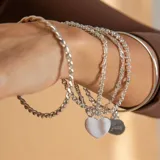 Brazalete tipo esclava de alambre redondo en plata 925, con dije de medalla circular colgante.