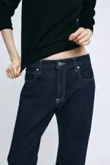 Jeans de tiro medio confeccionados en denim azul oscuro, con diseño de cinco bolsillos, trabillas para cinturón y bajo deshilachado. Cierre frontal con cremallera y botón metálico.