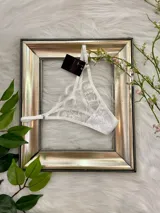 Tanga blanco de encaje con tiras regulables y refuerzo de algodón.