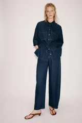 Camisa de denim azul oscuro con cuello solapa, mangas amplias por debajo del codo y bolsillos de parche en el frente. Cuenta con cintura ajustable mediante cordón y cierre frontal con botones metálicos.