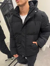 Campera puffer de nylon impermeable en color negro, con diseño acolchado, capucha forrada con corderito desmontable y cierre frontal con solapa.