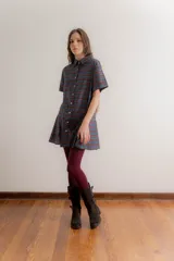 Vestido corto de estilo camisero con estampado de cuadros en tonos azul, verde y bordó. Presenta cuello clásico, cierre frontal con botones y falda tableada con corte a la cadera.