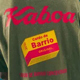 Remera verde militar de corte oversize con cuello redondo y estampado frontal con la frase "Caldo de Barrio" en letras rojas.