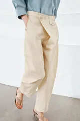 Pantalón de tiro medio confeccionado en algodón, con diseño cruzado en la cintura y cierre frontal con botones. Presenta trabillas para cinturón, bolsillos laterales ocultos y un bolsillo frontal con solapa y botón.