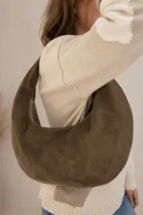 Cartera tipo hobo de gamuza color marrón chocolate, con diseño curvado, asa integrada para llevar al hombro y cierre superior.