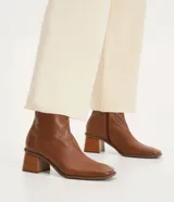 Bota de cuero de caña media para mujer, con punta cuadrada y tacón bloque de 6 cm. Presenta un cierre de cremallera en el lateral interno y una costura central decorativa en la parte frontal.