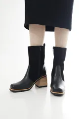 Bota de caña media combinada de cuero liso en la puntera y descarne en el resto de la caña, color negro. Cuenta con taco ancho con acabado de madera, suelaトラック y cierre lateral interno.