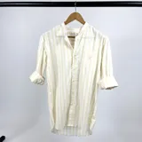 Camisa de algodón a rayas verticales color crema y blanco, con cuello mao y mangas largas con puños abotonados.