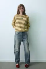 Camiseta oversize de manga larga con diseño de rayas horizontales amarillas y negras. Presenta cuello redondo y un detalle de texto bordado en el centro del pecho.